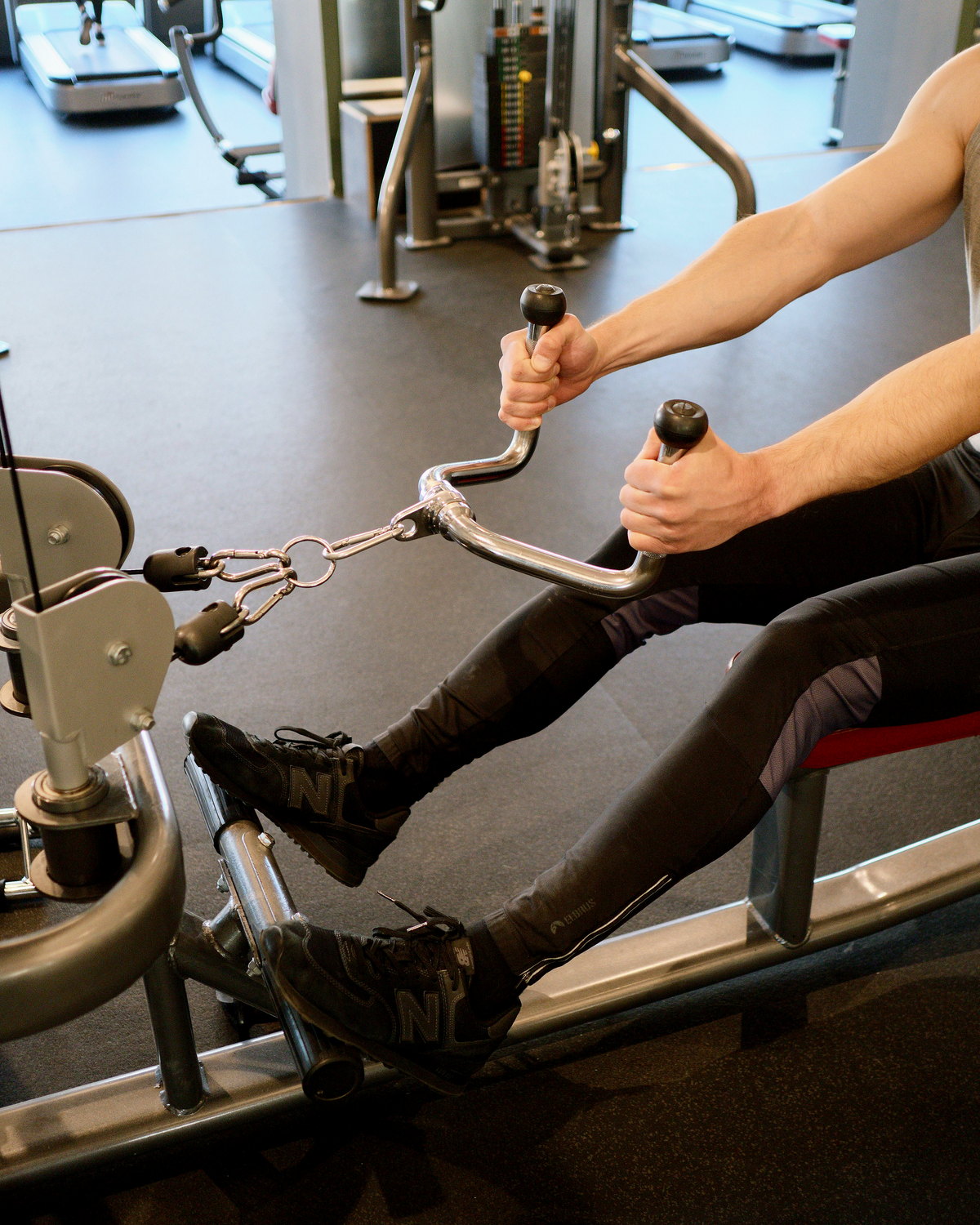 Person using a seated row machine in a gym, with treadmills visible behind.