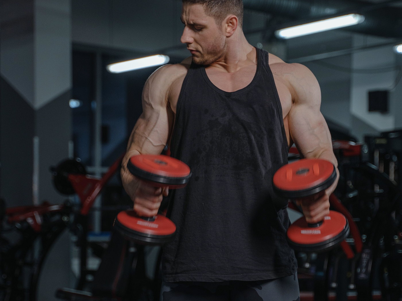 Man lifting red dumbbells in a gym, with weight machines behind him.